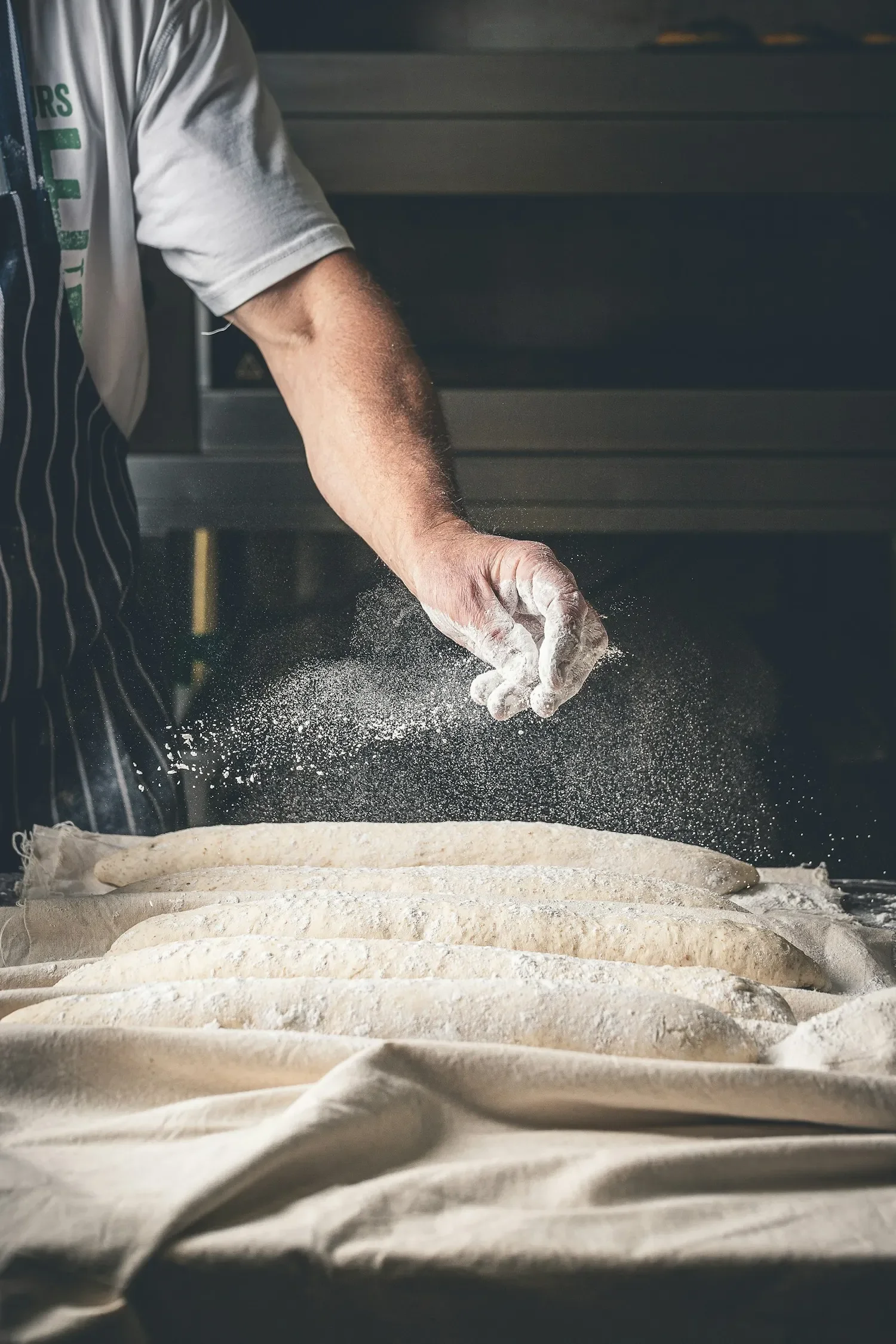 Hands dusting dough with flour by a dim oven